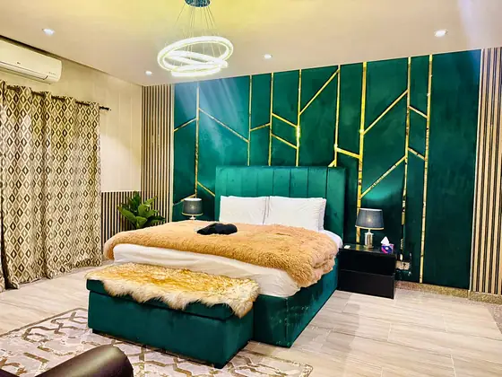 Beds dressed like a boutique hotel. Padded velvet headboards with brass inlay, faux-fur throws, ottomans, wall sconces and blackout curtains.